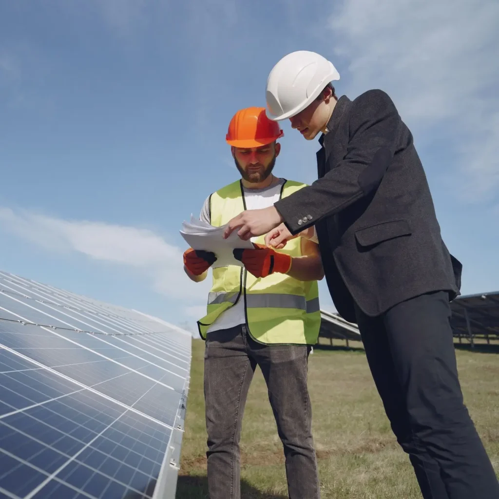 Dos técnicos con casco revisan planos junto a una instalación de placas solares